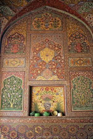 Intricate Mughal-era fresco artwork featuring detailed floral patterns, vibrant geometric borders, and traditional decorative motifs on the interior wall of a historic building in Lahore.