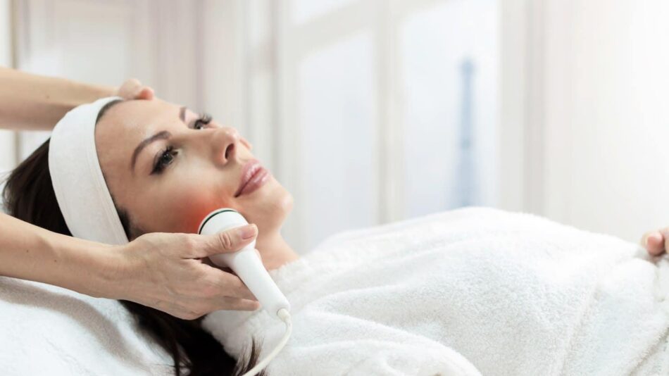 A woman receiving a professional facial treatment with a handheld skin-tightening device while lying comfortably on a spa bed.